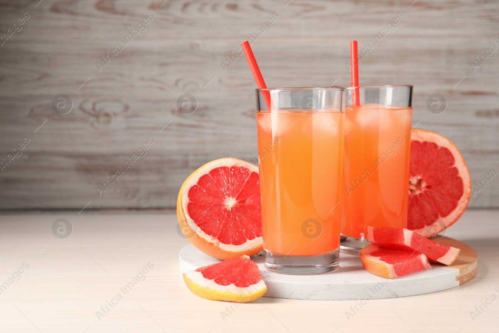 Photo of Tasty freshly made grapefruit juice and fruits on white wooden table, space for text