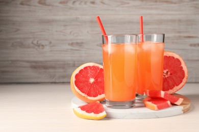 Tasty freshly made grapefruit juice and fruits on white wooden table, space for text