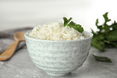 Photo of Bowl with tasty cooked rice and parsley on light grey marble table, closeup