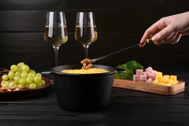 Photo of Woman dipping walnut into fondue pot with melted cheese at black wooden table, closeup
