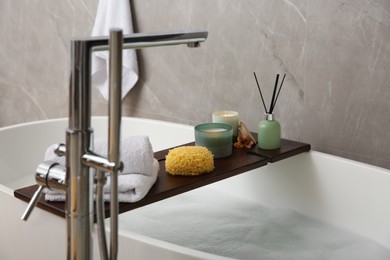 Photo of Wooden bath tray with candles, air freshener, towels and sponge on tub indoors