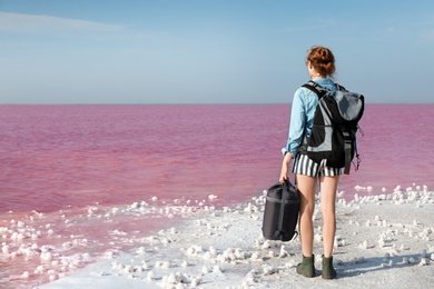 Woman with backpack and sleeping bag on coast of pink lake