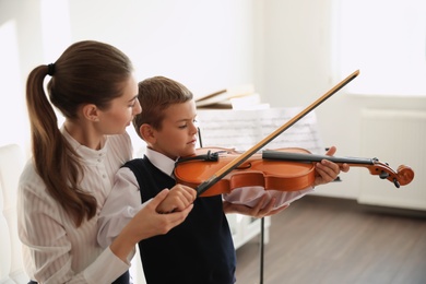 Young woman teaching little boy to play violin indoors