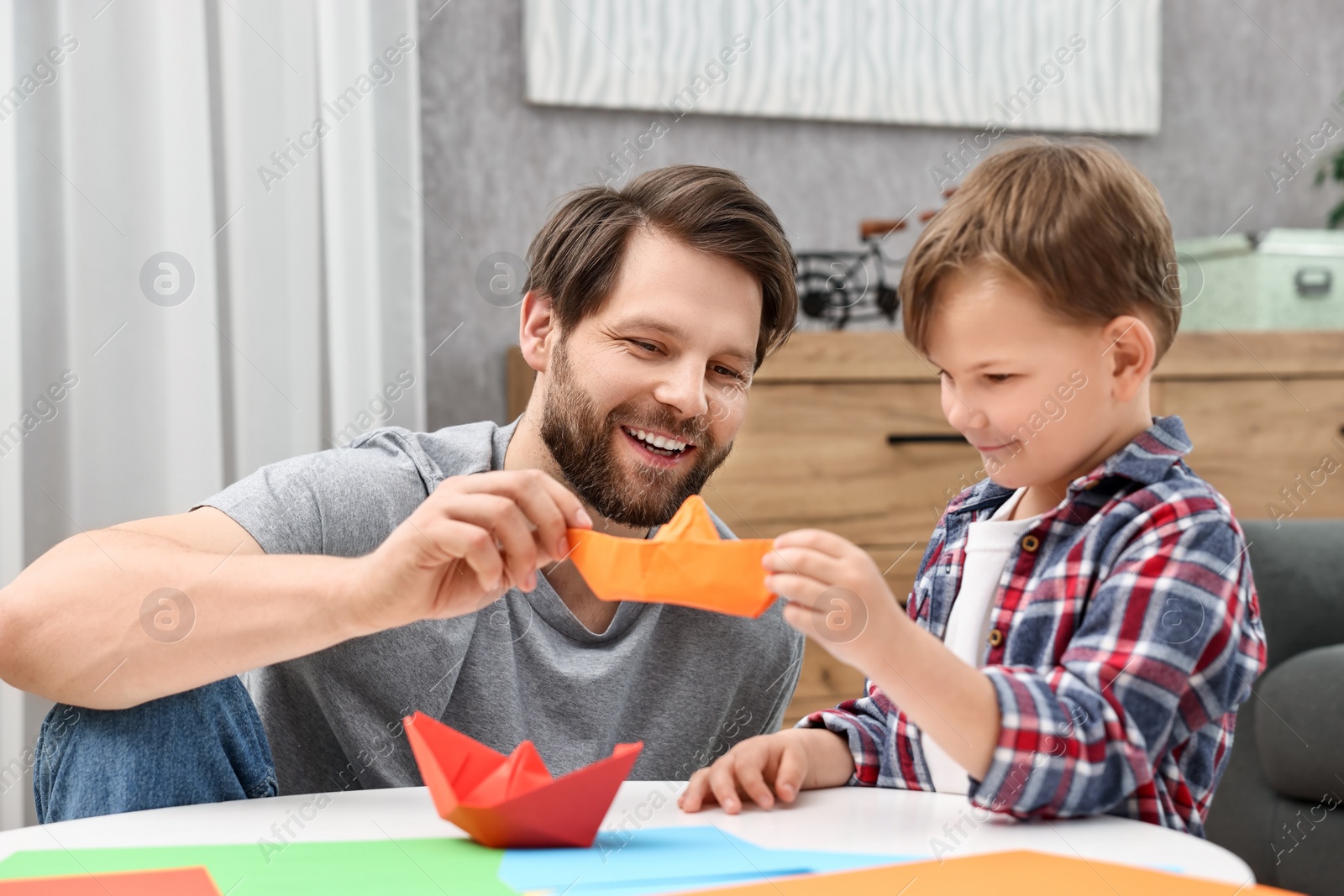 Photo of Dad and son making paper boats at coffee table indoors