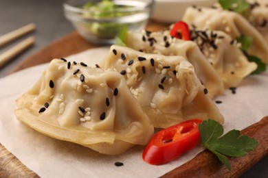 Photo of Delicious gyoza (asian dumplings) with sesame seeds and chili pepper on wooden board, closeup