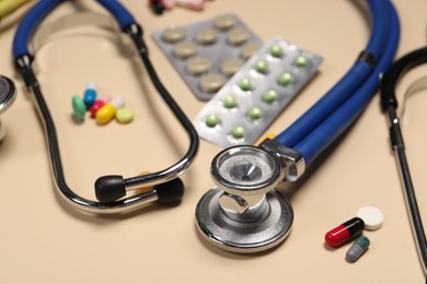 Stethoscope and pills on beige background, closeup. Medical tool