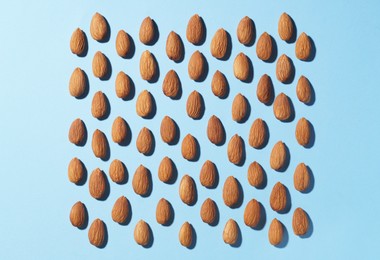 Photo of Delicious raw almonds on light blue background, flat lay