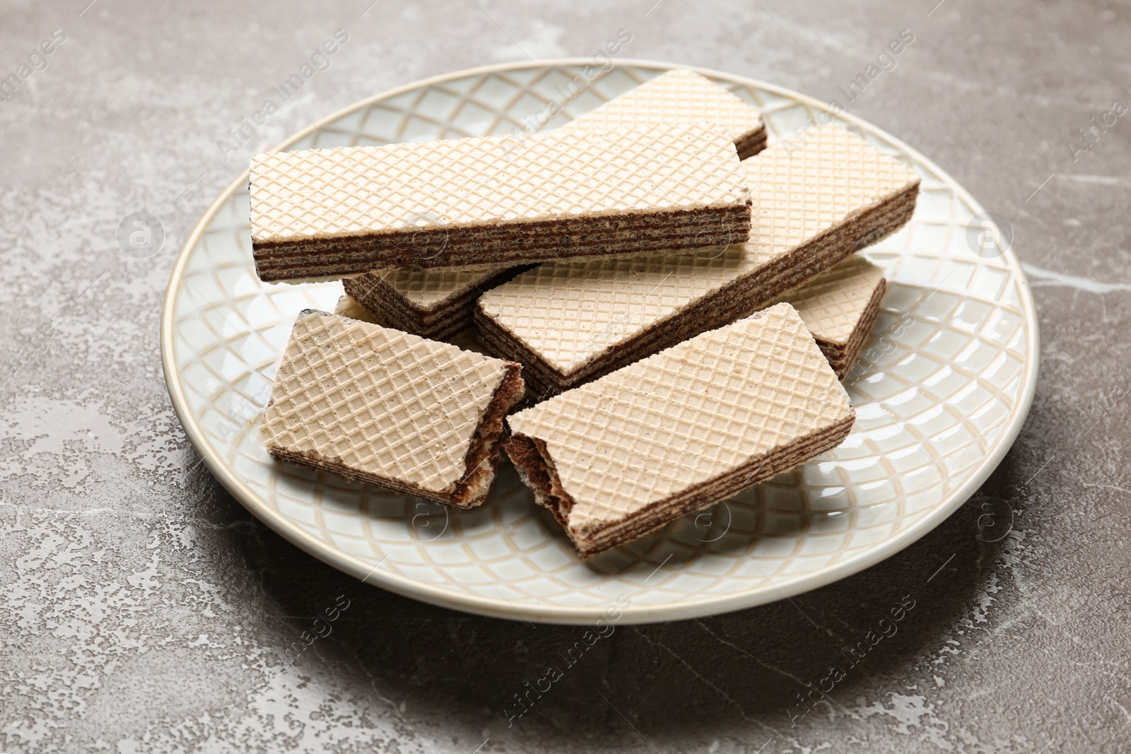 Photo of Plate of delicious crispy wafers with chocolate filling on grey stone table