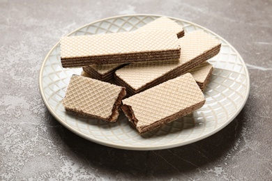 Photo of Plate of delicious crispy wafers with chocolate filling on grey stone table