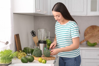 Photo of Young woman cutting broccoli for smoothie in kitchen