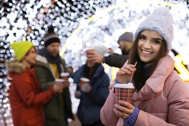 Photo of Happy woman with cup of mulled wine and friends at winter fair. Space for text
