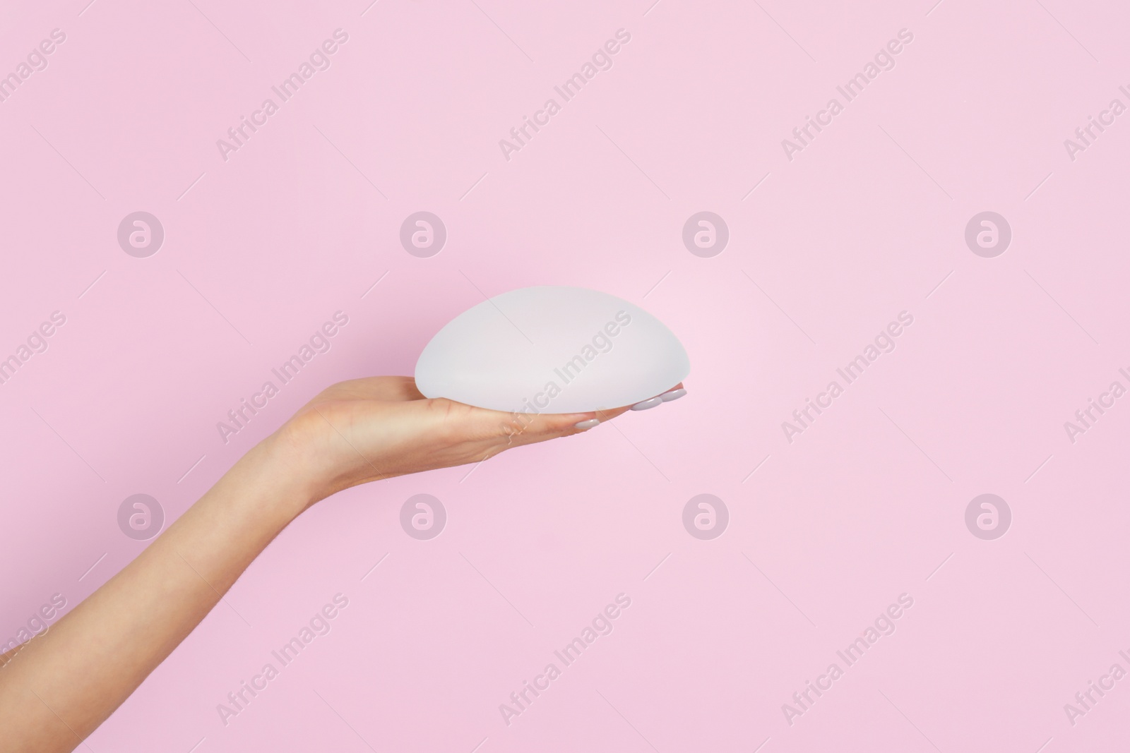 Photo of Woman holding silicone implant for breast augmentation on color background, space for text. Cosmetic surgery