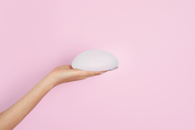 Photo of Woman holding silicone implant for breast augmentation on color background, space for text. Cosmetic surgery