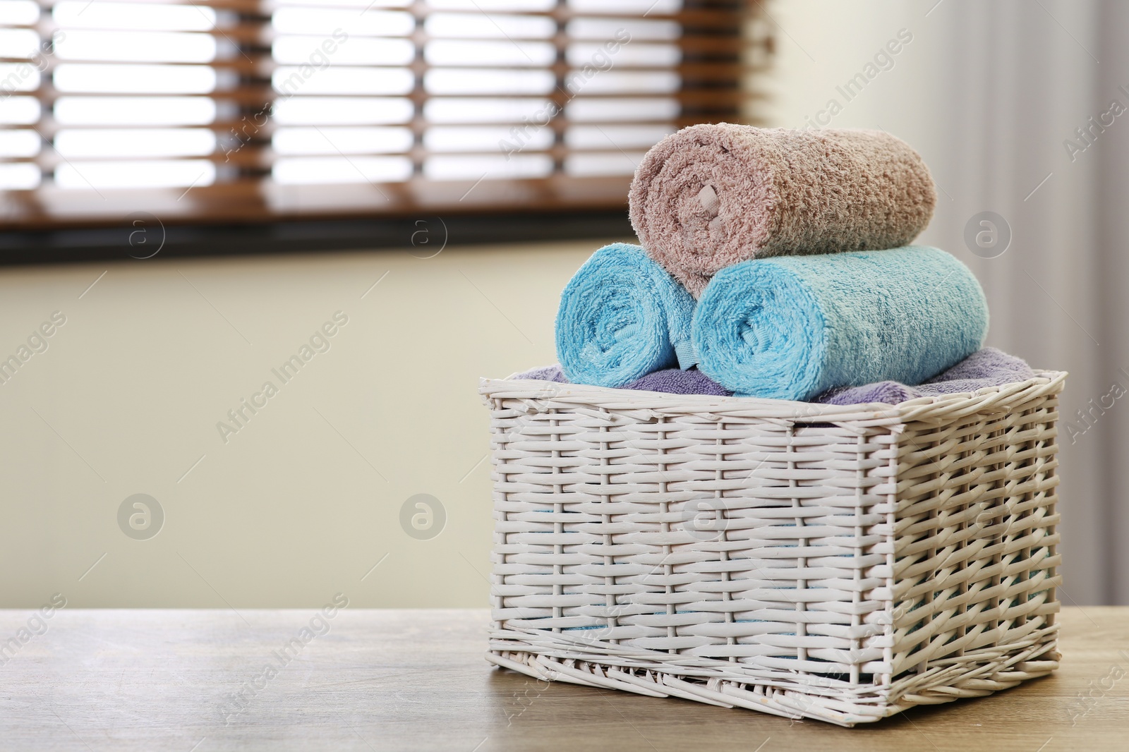 Photo of Wicker basket with clean towels on table indoors. Space for text