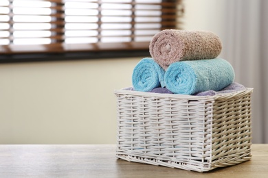 Photo of Wicker basket with clean towels on table indoors. Space for text