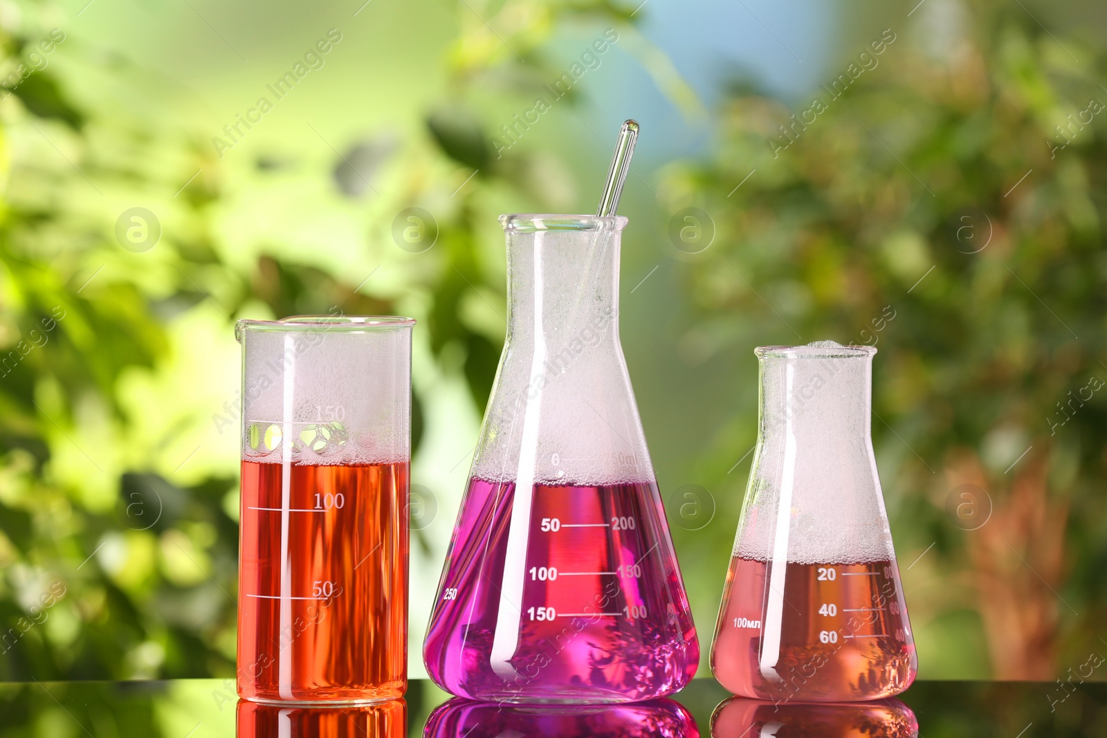 Photo of Laboratory glassware with colorful liquids on glass table outdoors. Chemical reaction