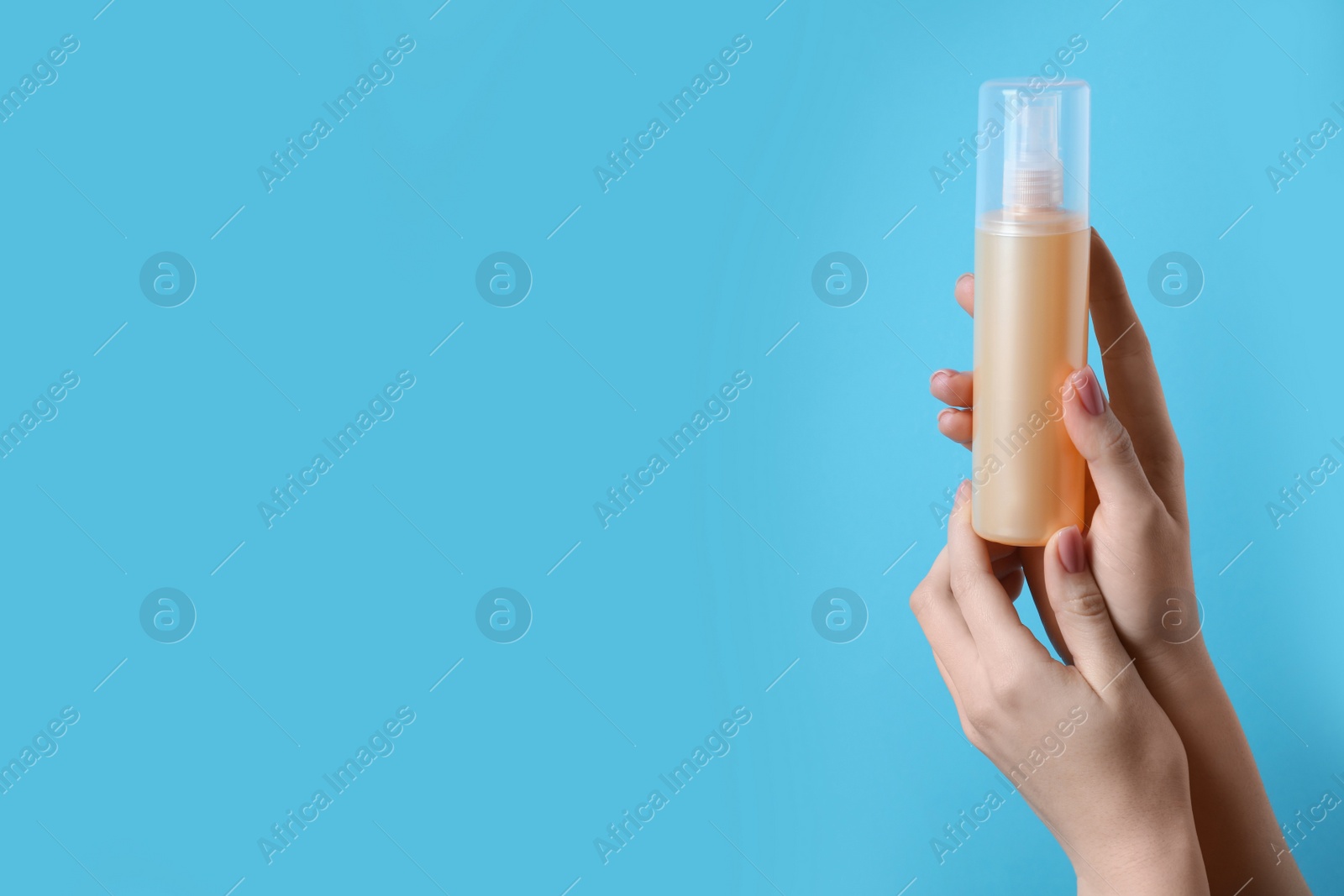 Photo of Woman holding spray bottle with thermal protection on light blue background, closeup. Space for text