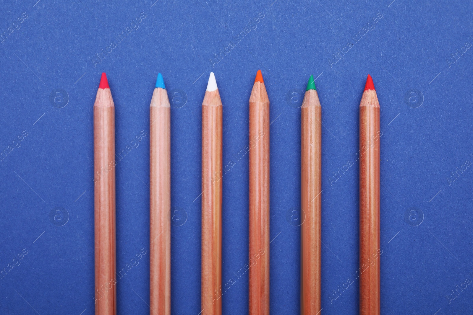 Photo of Colorful pastel pencils on blue background, flat lay. Drawing supplies