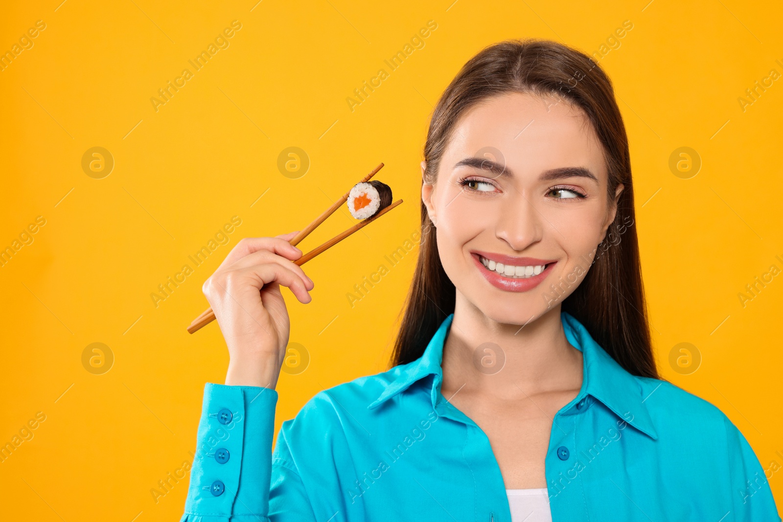 Photo of Happy beautiful young woman holding sushi roll with chopsticks on orange background