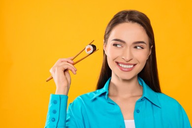 Photo of Happy beautiful young woman holding sushi roll with chopsticks on orange background