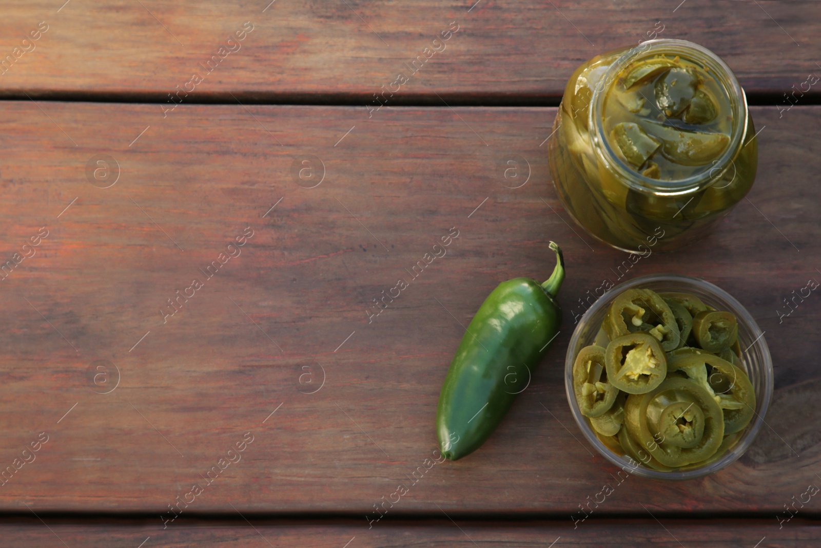 Photo of Fresh and pickled green jalapeno peppers on wooden table, flat lay. Space for text