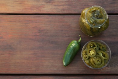 Photo of Fresh and pickled green jalapeno peppers on wooden table, flat lay. Space for text