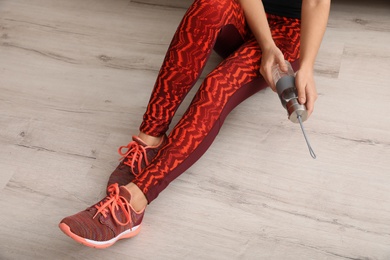 Photo of Woman in sportswear with bottle of water sitting on floor indoors. Space for text