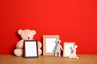 Photo of Soft toys and photo frames on table against red background, space for text. Child room interior