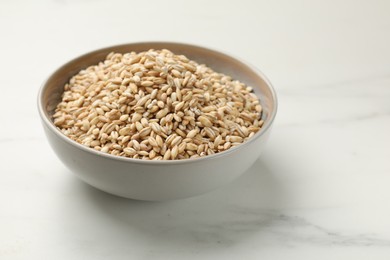 Photo of Dry pearl barley in bowl on white marble table, space for text