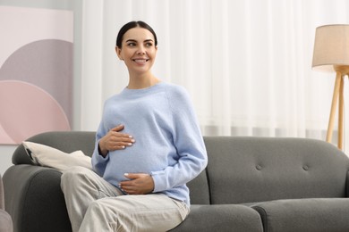 Happy pregnant woman on sofa at home, space for text