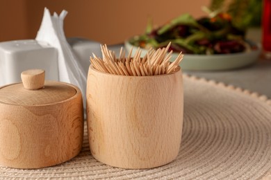 Photo of Wooden holder with many toothpicks on wicker mat, closeup. Space for text