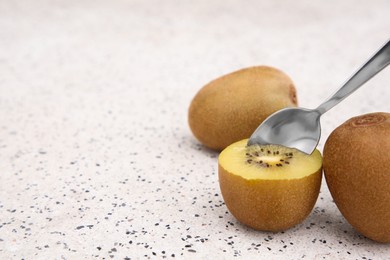 Photo of Spoon in fresh ripe yellow kiwi and fruits on white table with pattern. Space for text