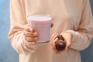 Woman holding smoothie and fresh figs on light blue background, closeup