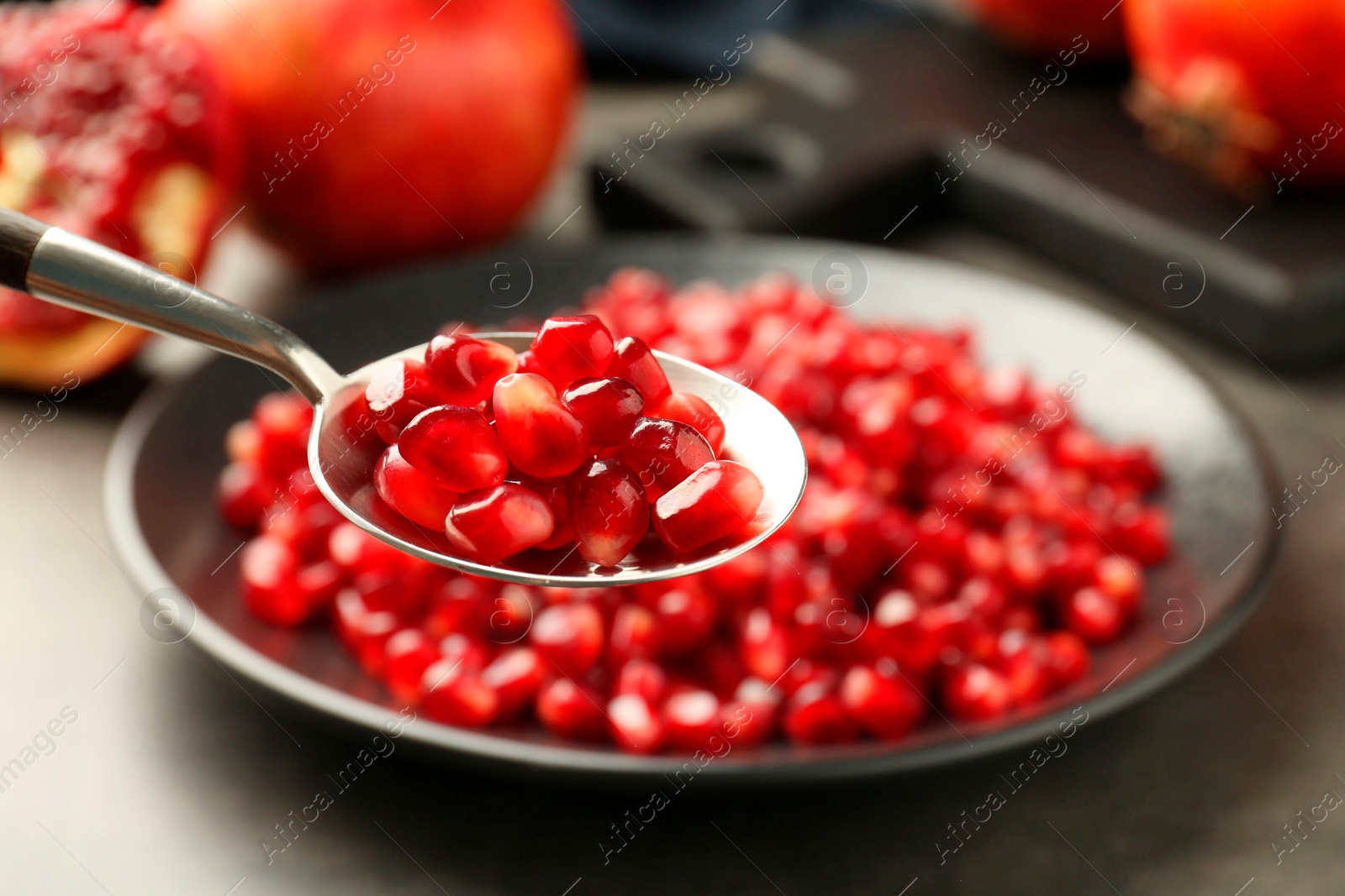 Photo of Eating ripe juicy pomegranate grains at grey table, closeup