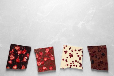 Photo of Different chocolate bars with freeze dried fruits on light marble table, flat lay. Space for text