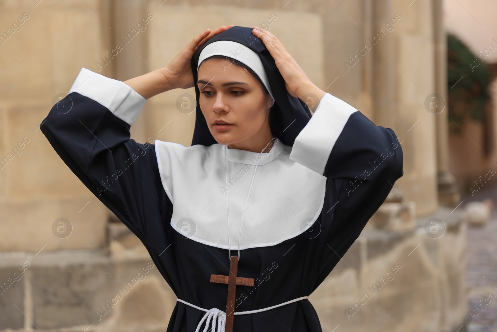 Photo of Young nun with Christian cross near building outdoors