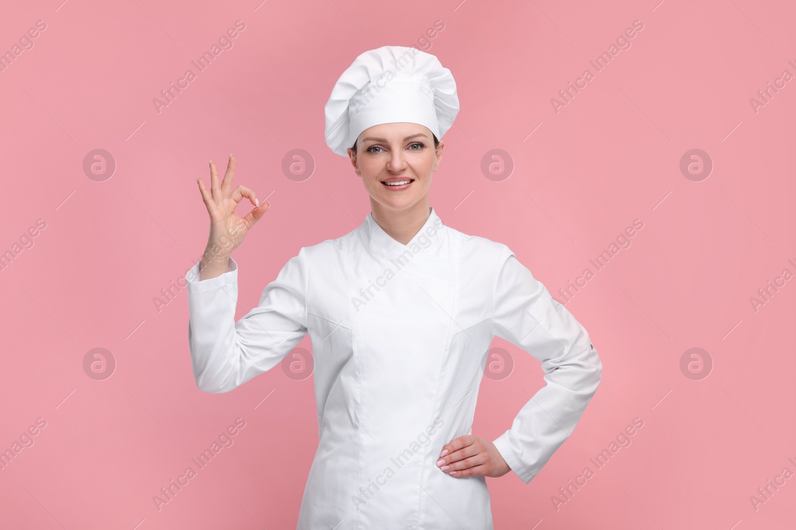 Photo of Happy chef in uniform showing OK gesture on pink background