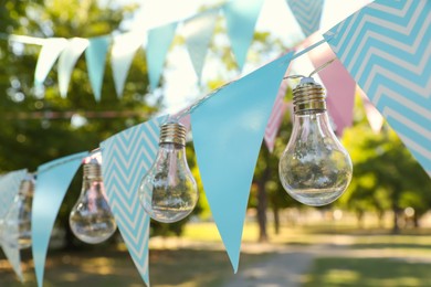 Photo of Colorful bunting flags with light bulbs in park. Party decor
