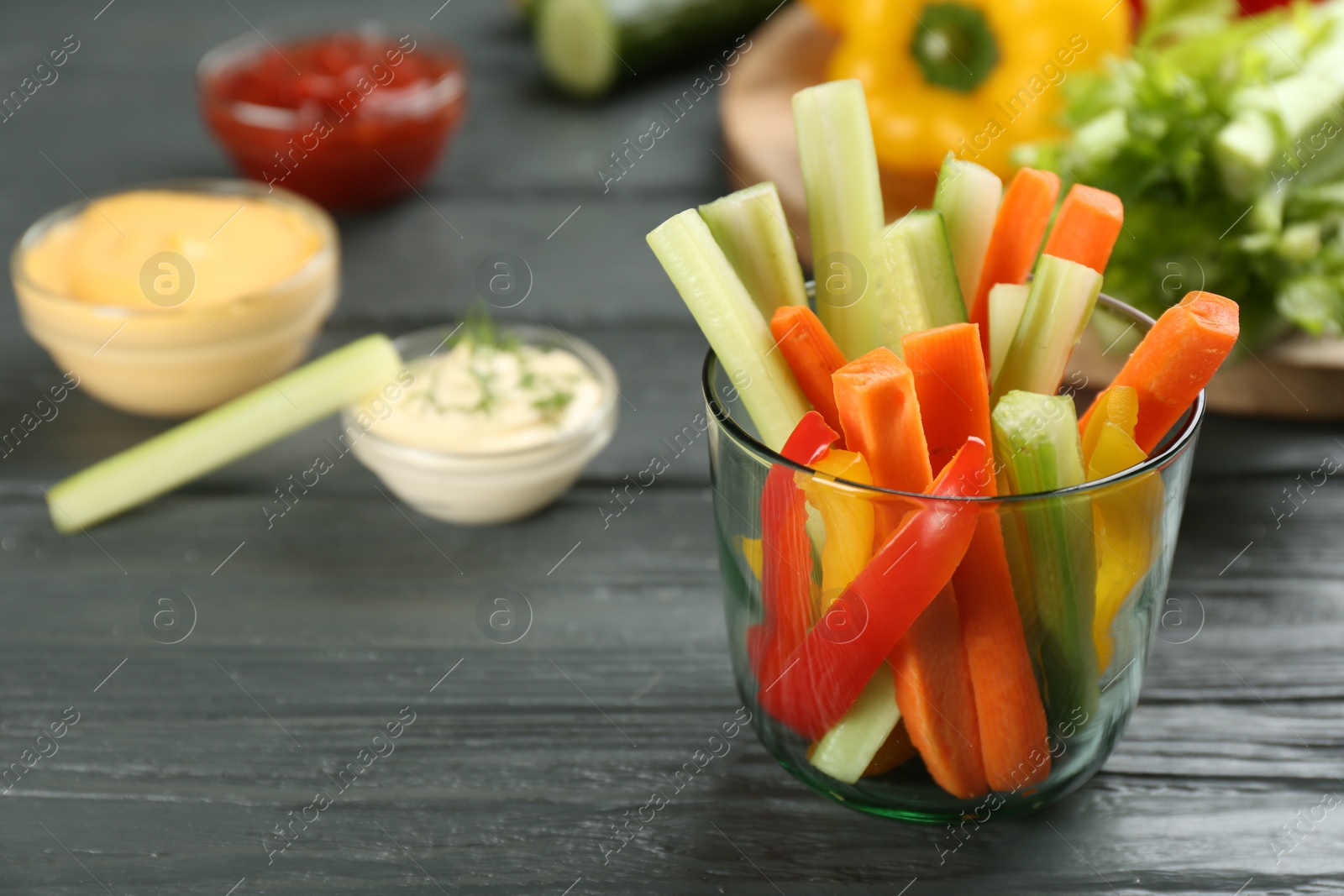 Photo of Celery and other vegetable sticks in glass on grey wooden table