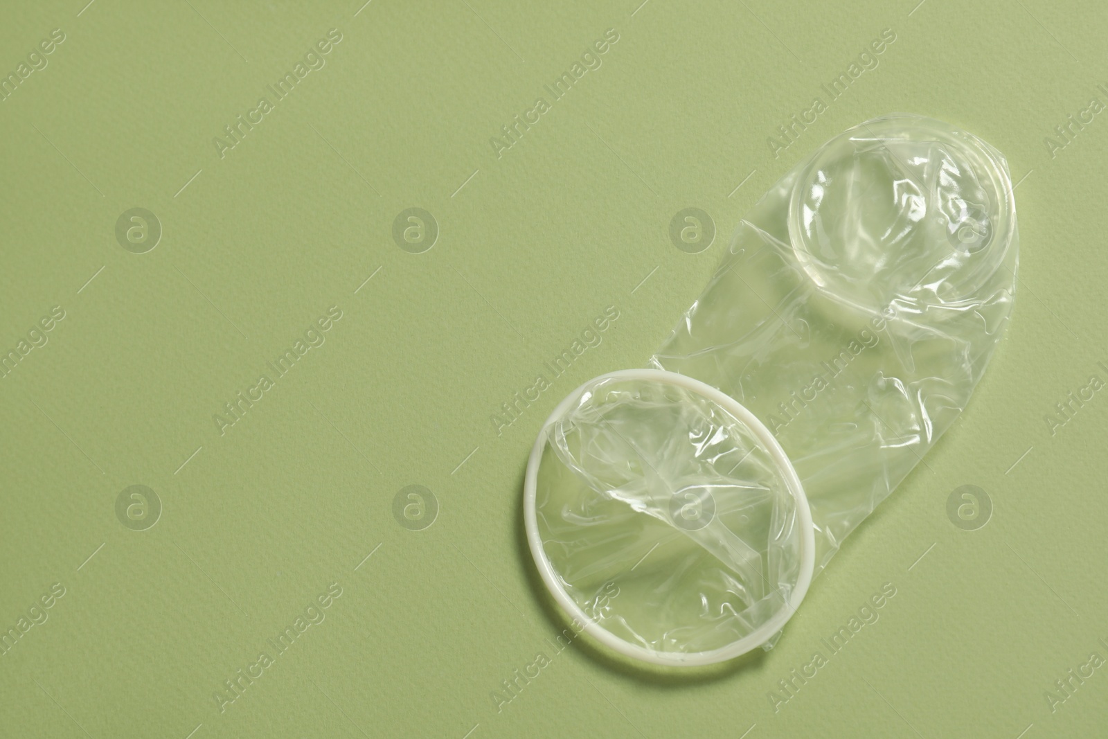 Photo of Unrolled female condom on light green background, top view and space for text. Safe sex