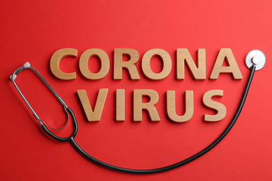 Photo of Words CORONA VIRUS made of wooden letters and stethoscope on red background, flat lay