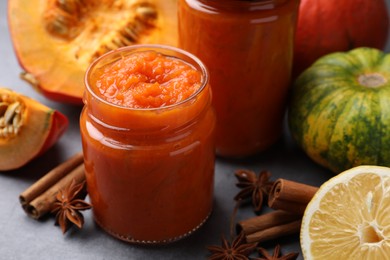 Jars of pumpkin jam and ingredients on grey table, closeup