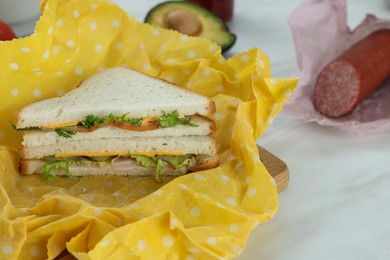 Photo of Tasty sandwich in beeswax food wrap on white marble table