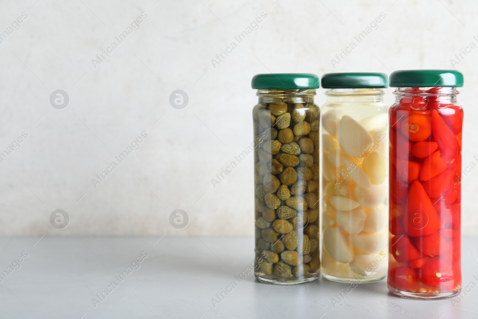 Photo of Jars with pickled vegetables on grey table against light background. Space for text