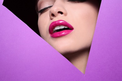 Photo of View of beautiful young woman with perfect lips makeup through cutout in color paper