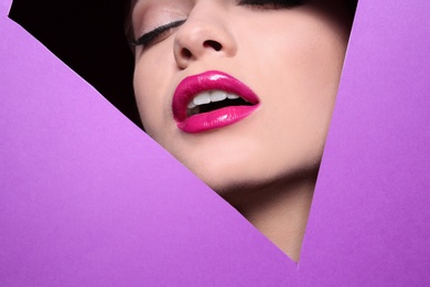 View of beautiful young woman with perfect lips makeup through cutout in color paper