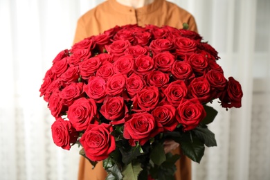 Photo of Woman holding luxury bouquet of fresh red roses indoors, closeup