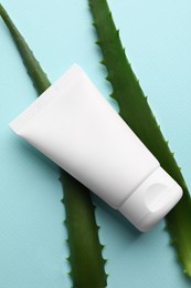 Photo of Tube of hand cream and aloe on turquoise background, flat lay