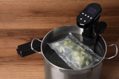 Photo of Thermal immersion circulator and vacuum packed broccoli in pot on wooden table. Sous vide cooking