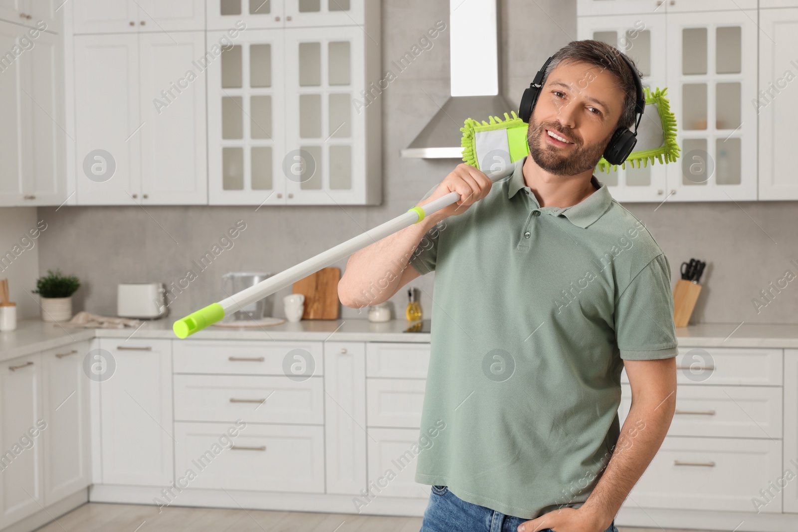 Photo of Happy man in headphones with mop in kitchen. Space for text